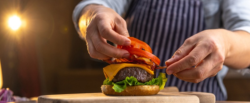 person adding tomatoes to a burger