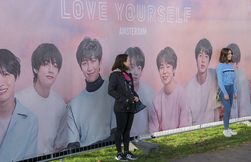 a woman posing in front of a billboard of BTS