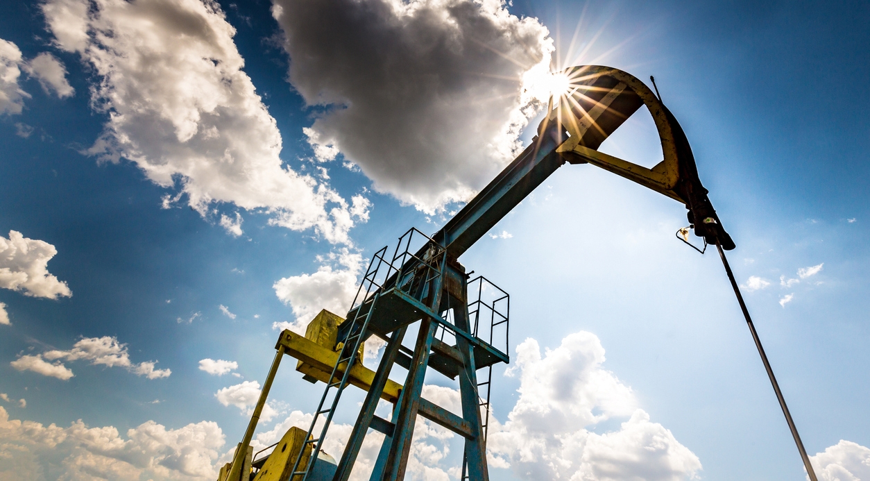 Oil field with pump jack, profiled on blue sky with white clouds