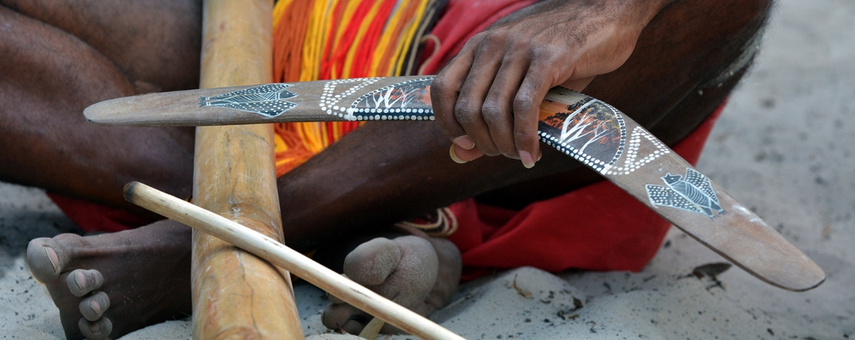 an Aboriginal man sitting and holding a boomerang and didgeridoo