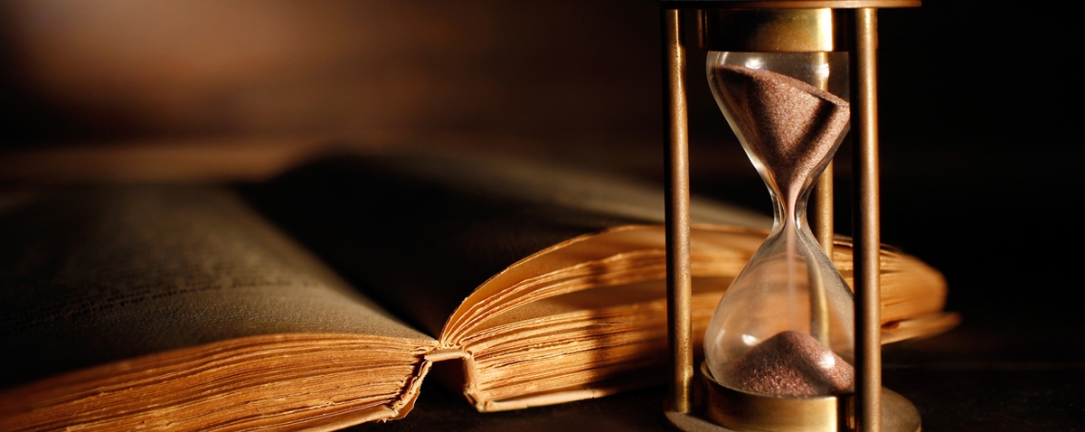 A hourglass by an ancient book on a table