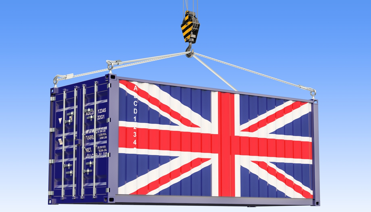 Cargo container with British flag hanging on the crane hook against blue sky