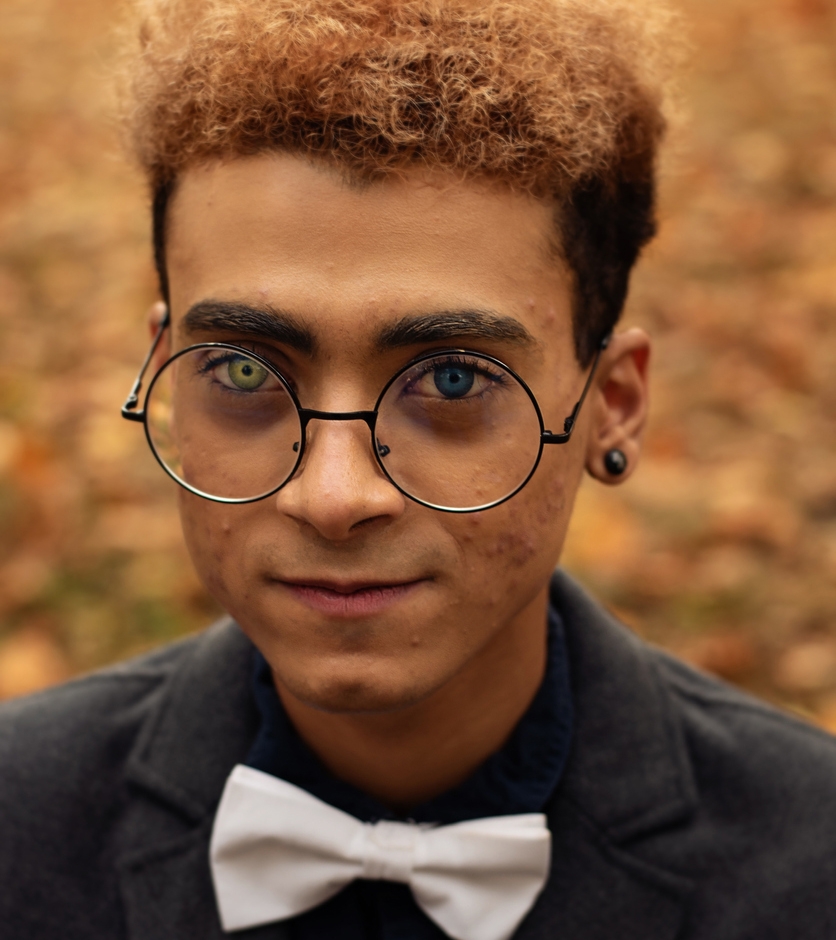 Handsome young African American man with heterochromia with round eyeglasses in park during fall season
